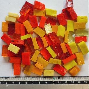 Könnte beinhalten: Sortiment kleiner, rechteckiger Glasfliesen in Gelb-, Orange- und Rottönen. Die Fliesen sind in einem zufälligen Muster auf einer weißen Oberfläche angeordnet.