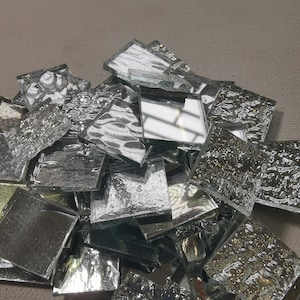 May include: A pile of silver mosaic tiles with a textured surface. The tiles are various sizes and shapes.