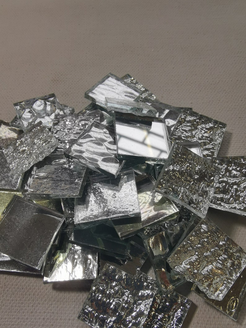 May include: A pile of silver mosaic tiles with a textured surface. The tiles are various sizes and shapes.