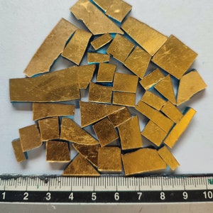 Puede incluir: Un montón de piezas de pan de oro, algunas con un respaldo azul, esparcidas sobre una superficie blanca. Una regla es visible en la parte inferior de la imagen, con marcas del 1 al 10.