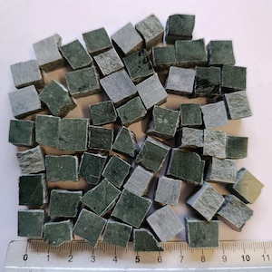 Può includere: Una collezione di piccole piastrelle quadrate in pietra verde e grigia. Le piastrelle sono di varie dimensioni e forme, con un righello che mostra le misure in centimetri. Le piastrelle sono probabilmente per progetti di mosaico o artigianato.