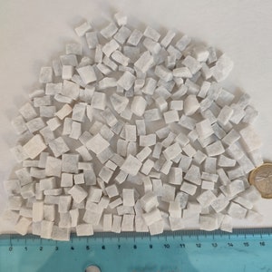 May include: A close-up of a pile of small, white marble chips. The chips are various sizes and shapes, and they are arranged in a random pattern. A ruler is visible at the bottom of the image, with markings from 0 to 16 inches.