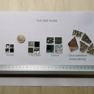 May include: Tile size guide showing four different sizes of silver mosaic tiles. The tiles are arranged in rows with labels indicating their dimensions in centimeters: 1x1cm, 1.5x1.5cm, 2x2cm, and Opus palladium (crazy paving). A ruler is included for reference.