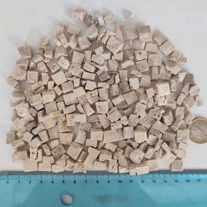 May include: A large pile of small, beige, square-shaped mosaic tiles. The tiles are arranged in a random pattern and are approximately 1/2 inch in size. A ruler is visible at the bottom of the image, with markings from 0 to 17 inches.