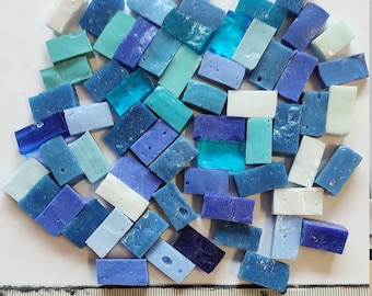 May include: A collection of small, rectangular glass tiles in various shades of blue, teal, and white. The tiles are arranged in a random pattern and are approximately 1 inch in length.