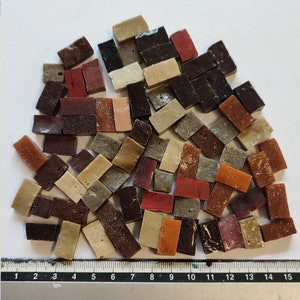Puede incluir: Una colección de pequeñas baldosas de mosaico rectangulares en varios tonos de marrón, rojo y beige. Las baldosas están dispuestas en un patrón aleatorio y tienen aproximadamente 2,5 cm de largo.