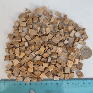 以下が含まれることがあります： 白っぽい背景に、不規則な形をした薄い茶色とベージュの小さな石のタイルが、たくさん積み重ねられています。タイルの大きさは約1.2cmで、ランダムに散らばっています。画像の下部には、0から16までの目盛りがついた定規が見えます。