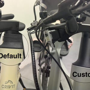 May include: Close-up of bicycle handlebars and frame, with the words "Default" and "Custom" in circles. The bike has black handlebars, a light, and a cream-coloured frame. The "Default" frame is cream, and the "Custom" frame is silver.