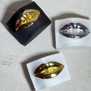 May include: Three decorative lips sculptures, one with gold, one with silver, and one with gold lips on a white background.