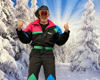 May include: A black ski suit with pink, green, and blue accents. The suit has a zipper closure and a belt. The person is wearing a black ski mask and goggles. The background is a snowy forest.