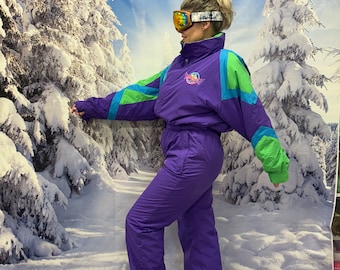 May include: A vintage purple ski suit with teal and green accents. The one-piece snowsuit has a high collar and is paired with ski goggles. The background is a winter scene with snow-covered trees.