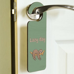 May include: Green door hanger with a sloth hanging from a branch. The text "Lazy day" is printed on the hanger.