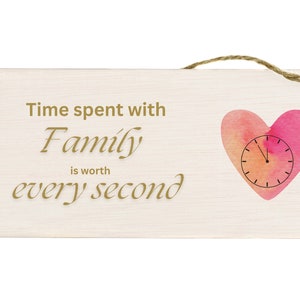 Op de afbeelding: Een houten bord met een roze en oranje aquarelhart met een wijzerplaat erin. Het bord staat: "Tijd doorgebracht met familie is elke seconde waard."