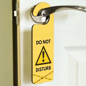 May include: Yellow door hanger with the text "DO NOT DISTURB" and a black exclamation point inside a black triangle. The hanger has black caution tape printed on the bottom.