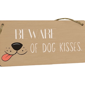 May include: A brown wooden sign with the text "BEWARE OF DOG KISSES."  A cartoon dog's nose and mouth with a pink tongue are printed on the sign.