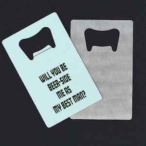 Puede incluir: Un abridor de botellas azul claro con el texto "Will you be beer-side me as my best man?" en verde oscuro. El abridor de botellas está al lado de un abridor de botellas plateado.