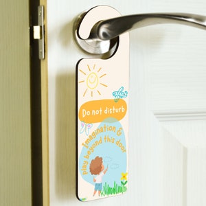 May include: A yellow and blue door hanger with a sun, airplane, and a child drawing on a cloud. The text reads "Do not disturb. Play imagination & beyond this door."