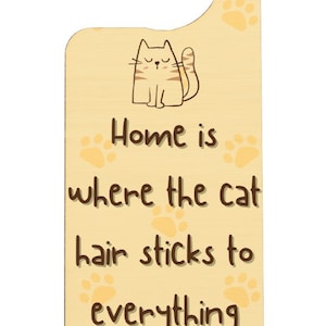 以下が含まれることがあります： 猫のイラストと「Home is where the cat hair sticks to everything」というテキストが書かれた、薄い黄色の木製ドアハンガーです。
