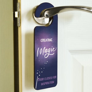 Puede incluir: Un colgador de puerta morado y azul con un fondo de noche estrellada. El texto en el colgador dice "Creating Magic" y "Door closed for inspiration".