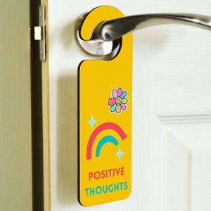 Może przedstawiać: Żółty wieszak na drzwi z tęczą, kwiatem z uśmiechniętą buźką i tekstem "POSITIVE THOUGHTS".