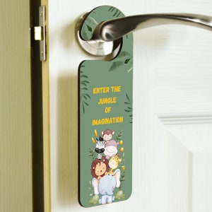 May include: A green wooden door hanger with a jungle theme. It features a cartoon elephant, lion, zebra, giraffe, and hippo. The text on the hanger reads "Enter the Jungle of Imagination".