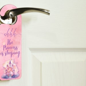 May include: Pink door hanger with a watercolor castle and clouds. The text reads "shhh The Princess is Sleeping".