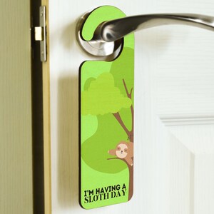 May include: A green door hanger with a cartoon sloth hanging from a tree. The text on the hanger reads "I'm having a sloth day."