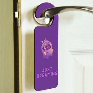 Może przedstawiać: Fioletowy wieszak na drzwi z grafiką głowy z galaktyką w środku i tekstem "JUST DREAMING".