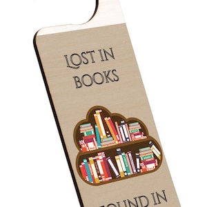 May include: A wooden door hanger with a brown background and a white hook. The hanger has a graphic of a bookshelf filled with colorful books. The text "LOST IN BOOKS FOUND IN LIBRARIES." is printed on the hanger.