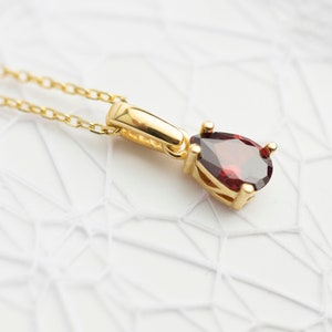 May include: A gold chain necklace with a pendant featuring a teardrop-shaped red gemstone.