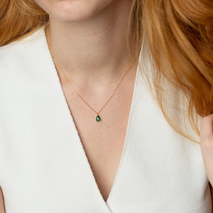 May include: A delicate gold chain necklace with a small, teardrop-shaped green gemstone pendant.