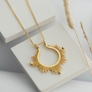 May include: A gold necklace featuring a sunburst pendant. The pendant is a circle with radiating lines and three small gold beads.