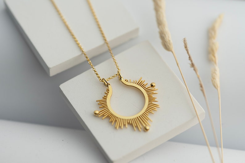May include: A gold necklace featuring a sunburst pendant. The pendant is a circle with radiating lines and three small gold beads.