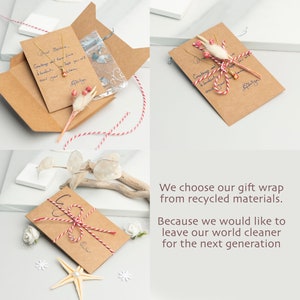 May include: A brown paper envelope with a red and white twine bow. The envelope has a handwritten message that says "Dear Martha. Greetings and love from Honolulu. Hope you will wear your..." The envelope is sitting on a white surface with a white starfish and white flowers.