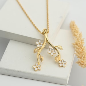 May include: A gold necklace with a pendant featuring a delicate branch with white flowers. The pendant is a stylised representation of a blossoming tree.