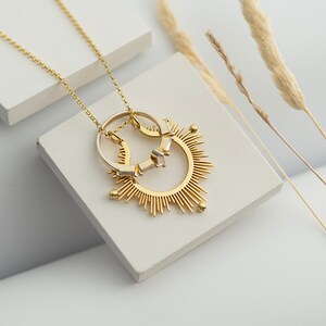 May include: A gold necklace featuring a sunburst pendant with two rings attached. The rings are made of gold and silver.