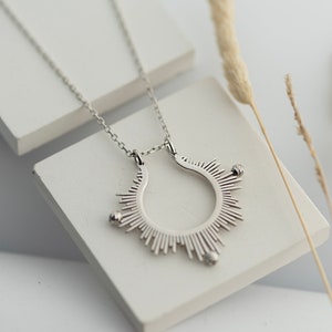 May include: A silver necklace featuring a sunburst pendant. The pendant is a circle with rays radiating outwards, each ending in a small bead.