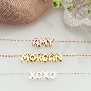 Könnte beinhalten: Drei goldene Halsketten mit verschiedenen Namen. Die oberste Halskette sagt "AMY" in Roségold, die mittlere Halskette sagt "MORGAN" in Gelbgold und die unterste Halskette sagt "XOXO" in Silber.