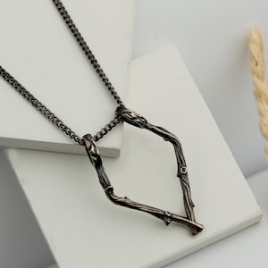 May include: A black chain necklace with a pendant shaped like a diamond made of two intertwined branches.