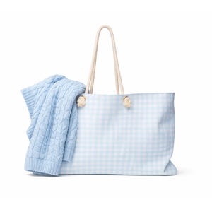 May include: A light blue and white gingham tote bag with rope handles. A light blue cable knit sweater is draped over the side of the bag. The bag is a large size, ideal for carrying essentials.