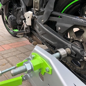 Pode incluir: Uma motocicleta verde e preta com um suporte de motocicleta de metal prateado. A motocicleta tem uma transmissão por corrente e uma roda verde com um pneu preto.