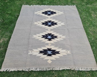May include: A rectangular area rug featuring a light grey base with four repeating diamond-shaped geometric patterns in black, cream, and light blue. The rug has a woven texture and is finished with short, straight fringe along the top and bottom edges.