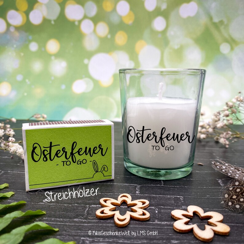 May include: A green matchbox with the text "Osterfeuer - TO GO -" and the word "Streichholzer" below. A small glass jar with a white candle inside and the text "Osterfeuer TO GO" on the side.