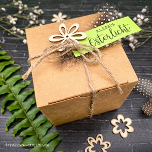 May include: A brown cardboard gift box tied with twine and decorated with a wooden flower and a green tag that reads "kleines Osterlicht".
