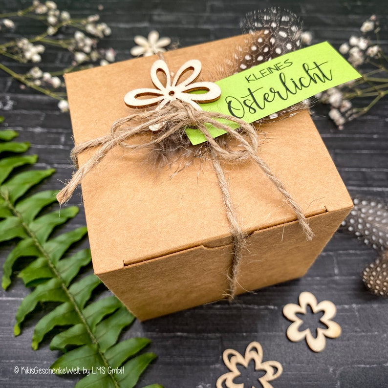 May include: A brown cardboard gift box tied with twine and decorated with a wooden flower and a green tag that reads "kleines Osterlicht".