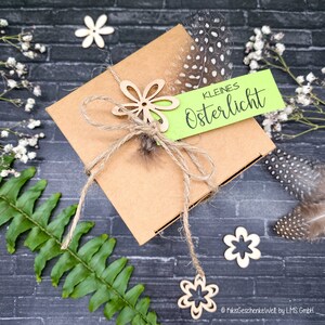 May include: A brown gift box tied with twine and decorated with wooden flowers and a green tag that reads "Kleines Osterlicht".