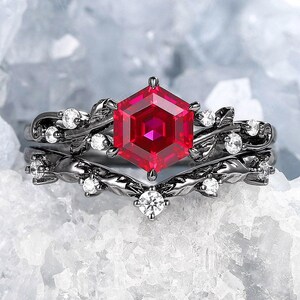 May include: A black ring set with a large, red hexagonal gemstone surrounded by smaller white gemstones. The ring features a delicate, vine-like design.