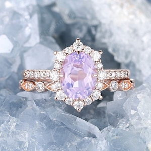 May include: A rose gold engagement ring set with a large oval amethyst center stone surrounded by smaller diamonds. The ring is set on a bed of blue crystals.