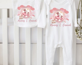 May include: White baby bib and onesie set. The bib and onesie feature a pink and white graphic of two mice in tutus, with the text "Mummy & Amavah". The set is hanging on a wooden hanger.