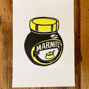 May include: A black and yellow illustration of a Marmite jar with the text "Marmite" and "100%" on the label. The text "Love it" is written below the jar.
